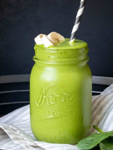 A glass jar with a green smoothie and straw in it