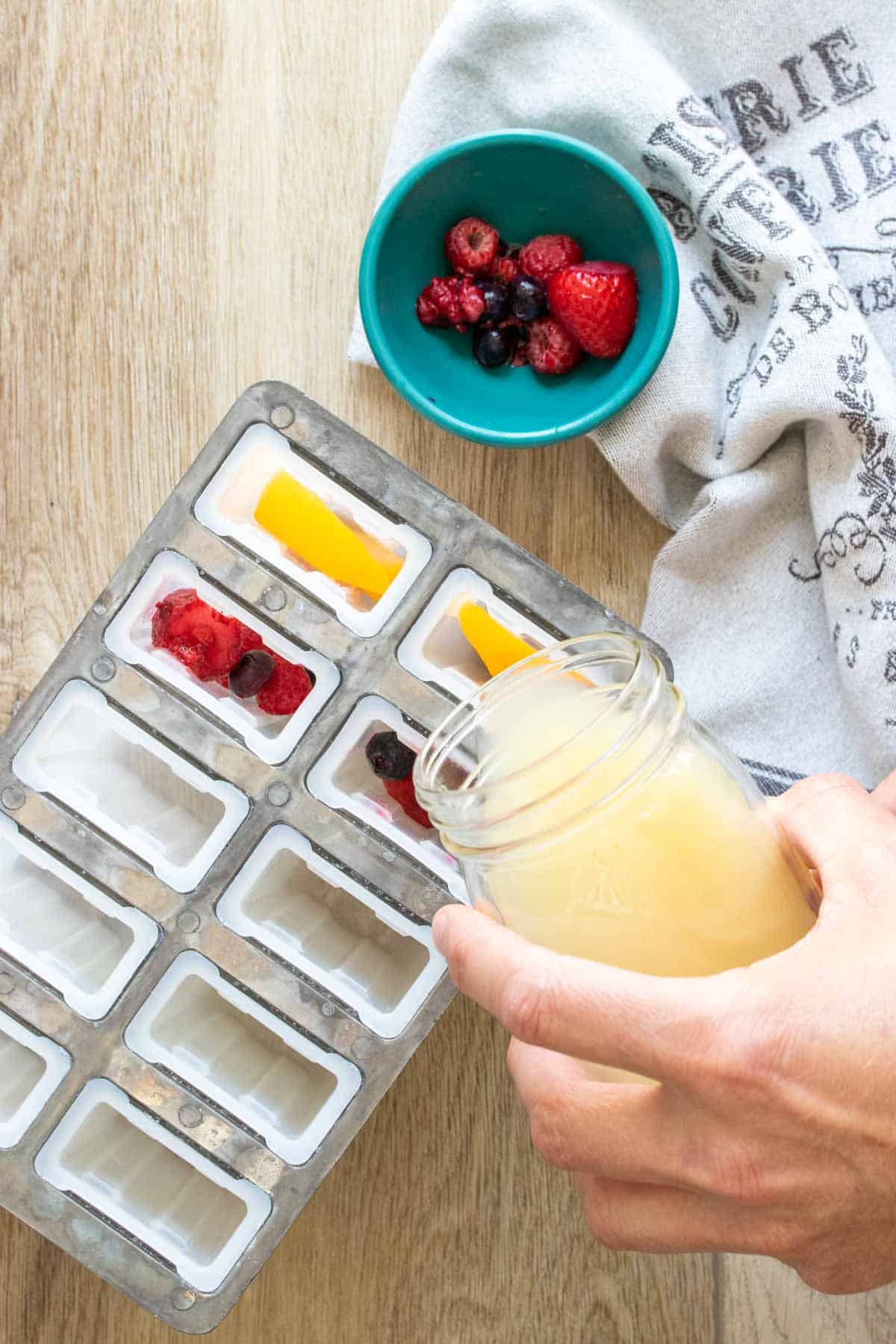 Hand pouring juice into a popsicle mold with a glass jar