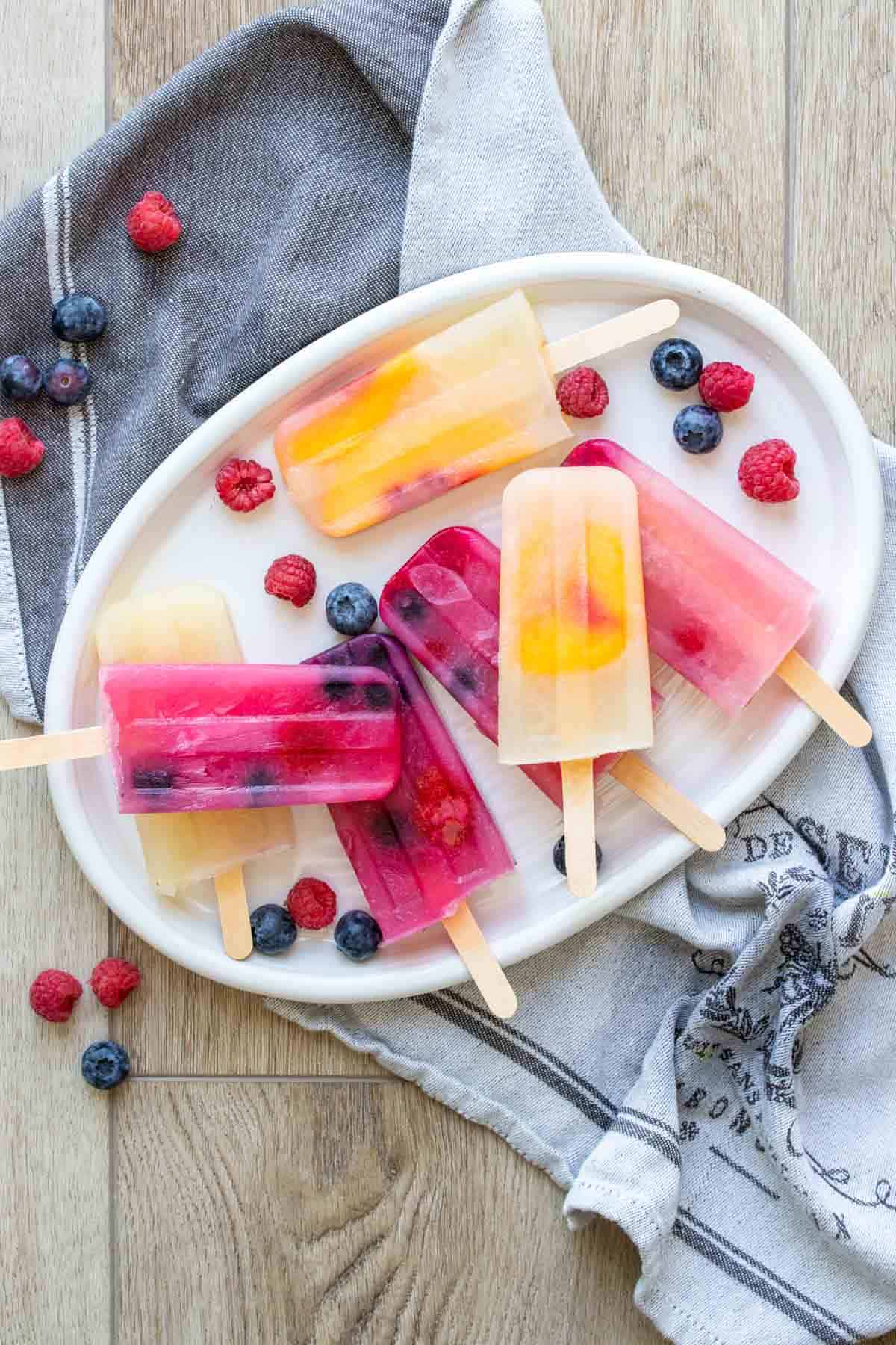 White platter with orange yellow and pink popsicles on it surrounded by berries