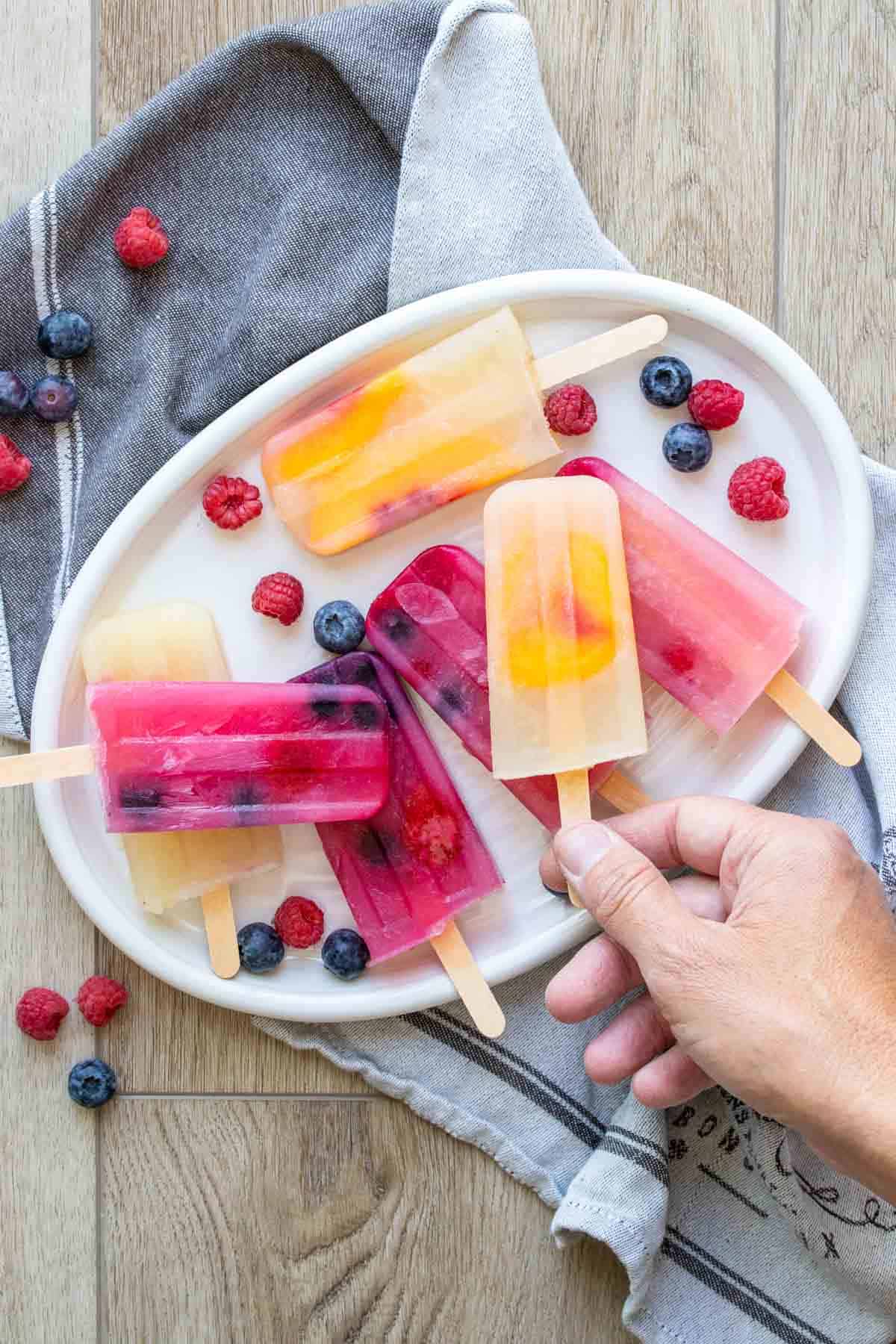 Hand taking a popsicle from a pile of them on white platter