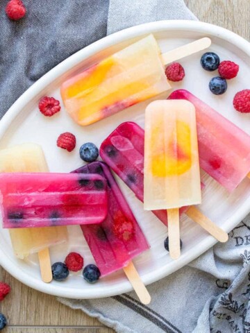 A white platter with a pile of yellow orange and pink popsicles with fruit inside of them on it