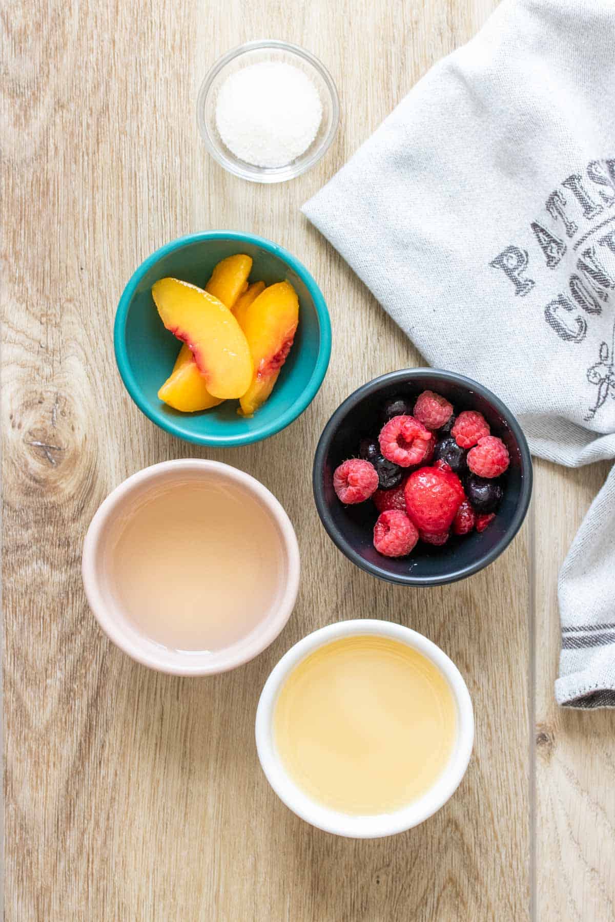 Bowls of fruit, wine and lemon juice on a wooden surface next to a towel