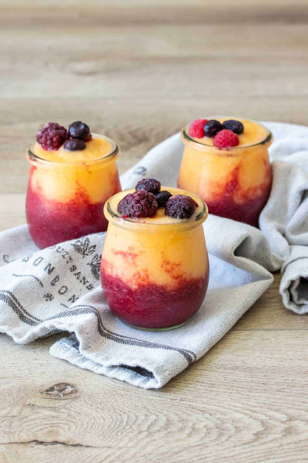 Three jars with multi colored wine slushies inside topped with berries