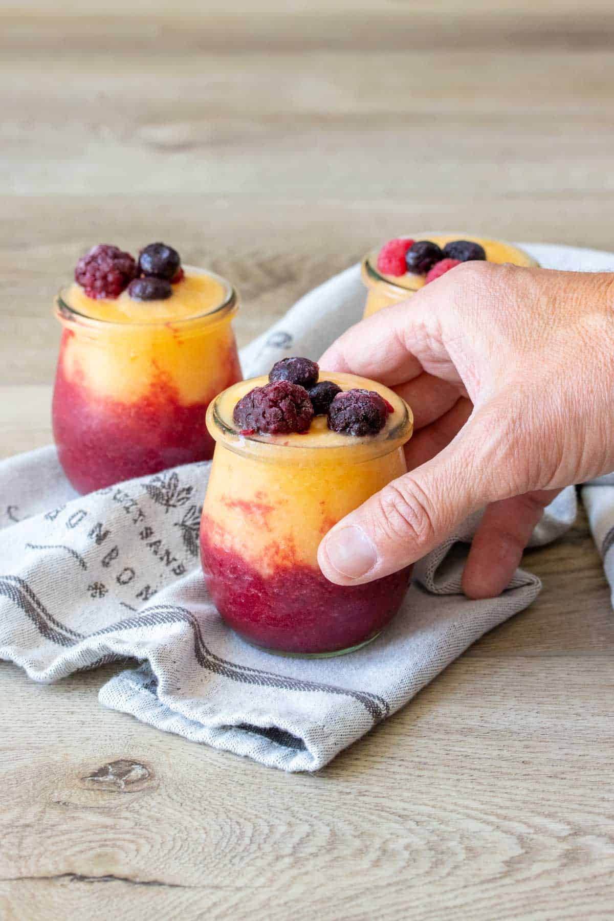 Hand grabbing a jar filled with a wine slushie topped with fruit