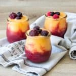 Three glass jars filled with two colors of wine slushies topped with fruit