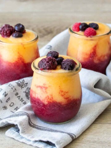 Three glass jars filled with two colors of wine slushies topped with fruit