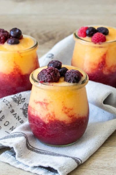Three glass jars filled with two colors of wine slushies topped with fruit