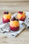 A photo of three frozen drinks topped with fruit in glass jars sitting on a grey towel.