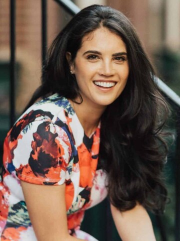 Woman with long black hair wearing a flower print dress smiling at the camera