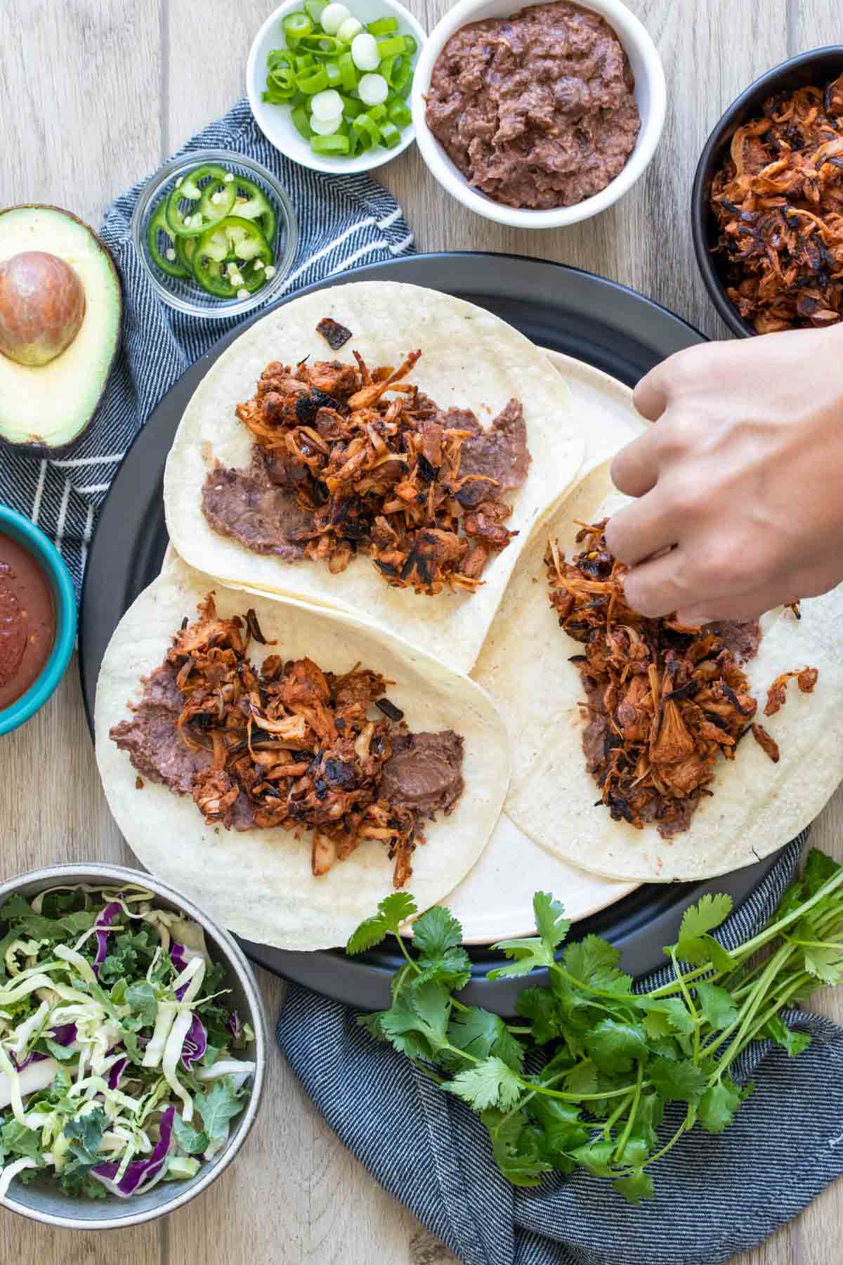 A hand putting jackfruit taco filling on tortillas with beans.