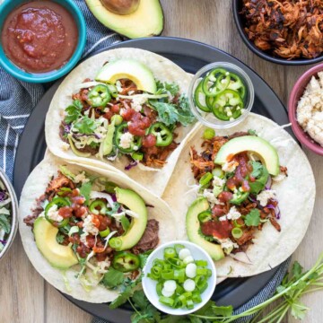 Three jackfruit tacos with toppings on a plate surrounded by ingredients
