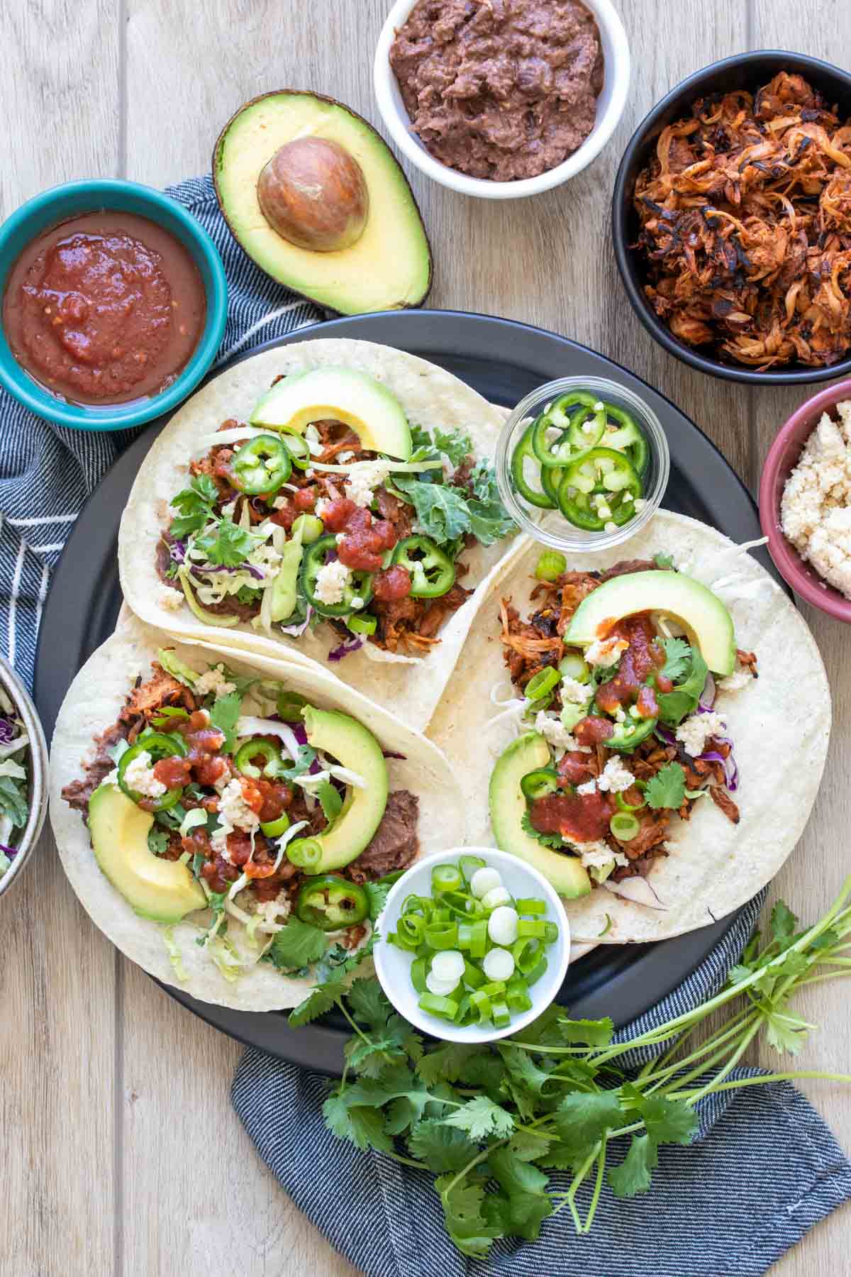 Three jackfruit tacos with toppings on a plate surrounded by ingredients.