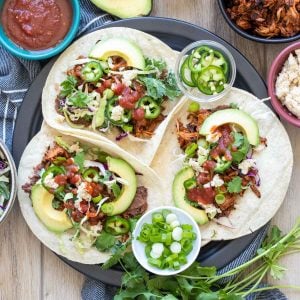 Three jackfruit tacos with lots of toppings on a black plate.