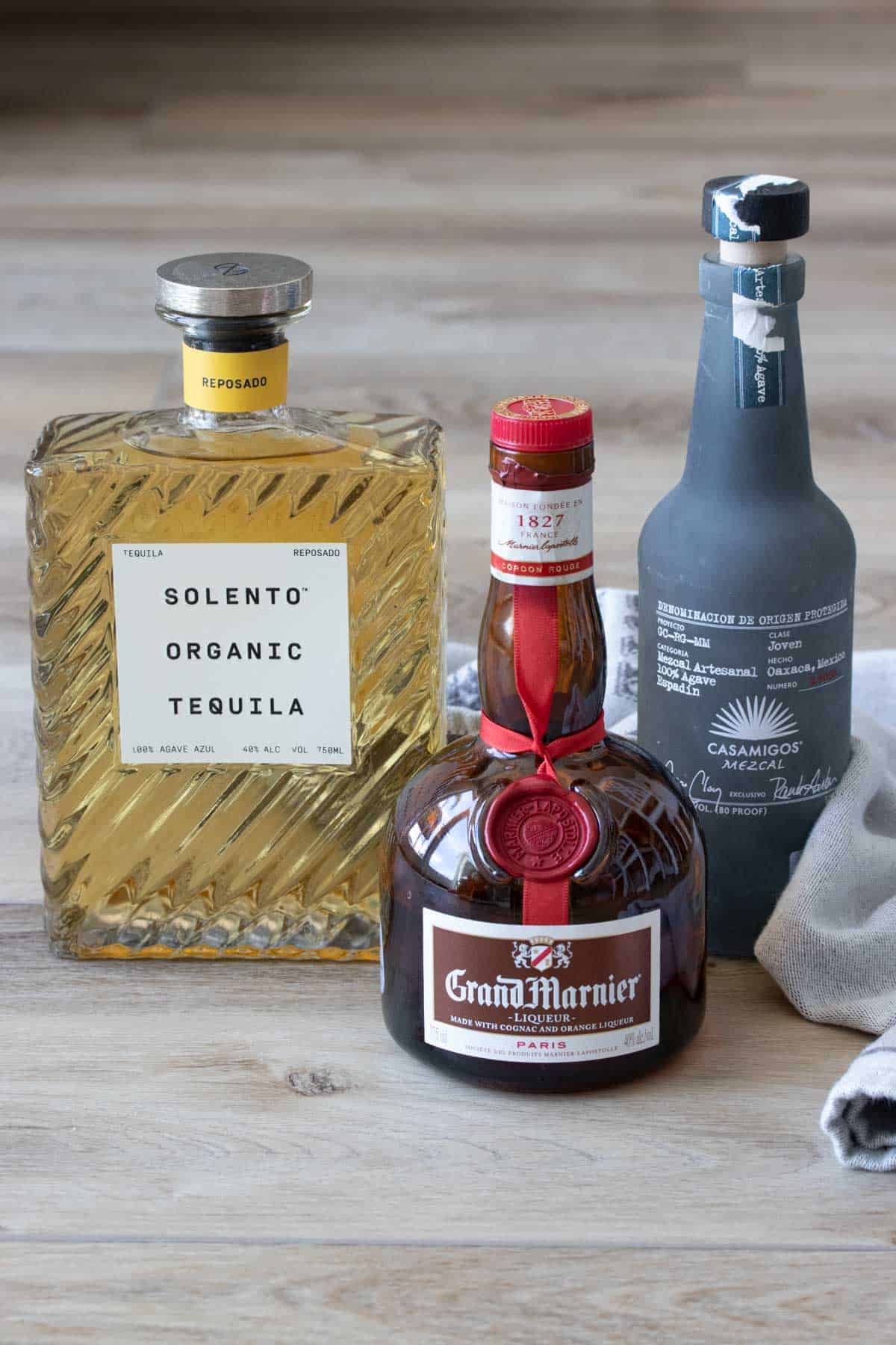Three bottles of alcohol sitting on a wooden surface