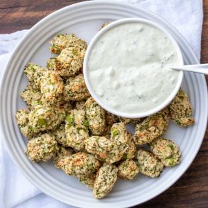 A white plate with veggie tots and a bowl of creamy chive dip on it.