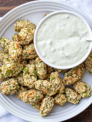 A white plate with veggie tots and a bowl of creamy chive dip on it.