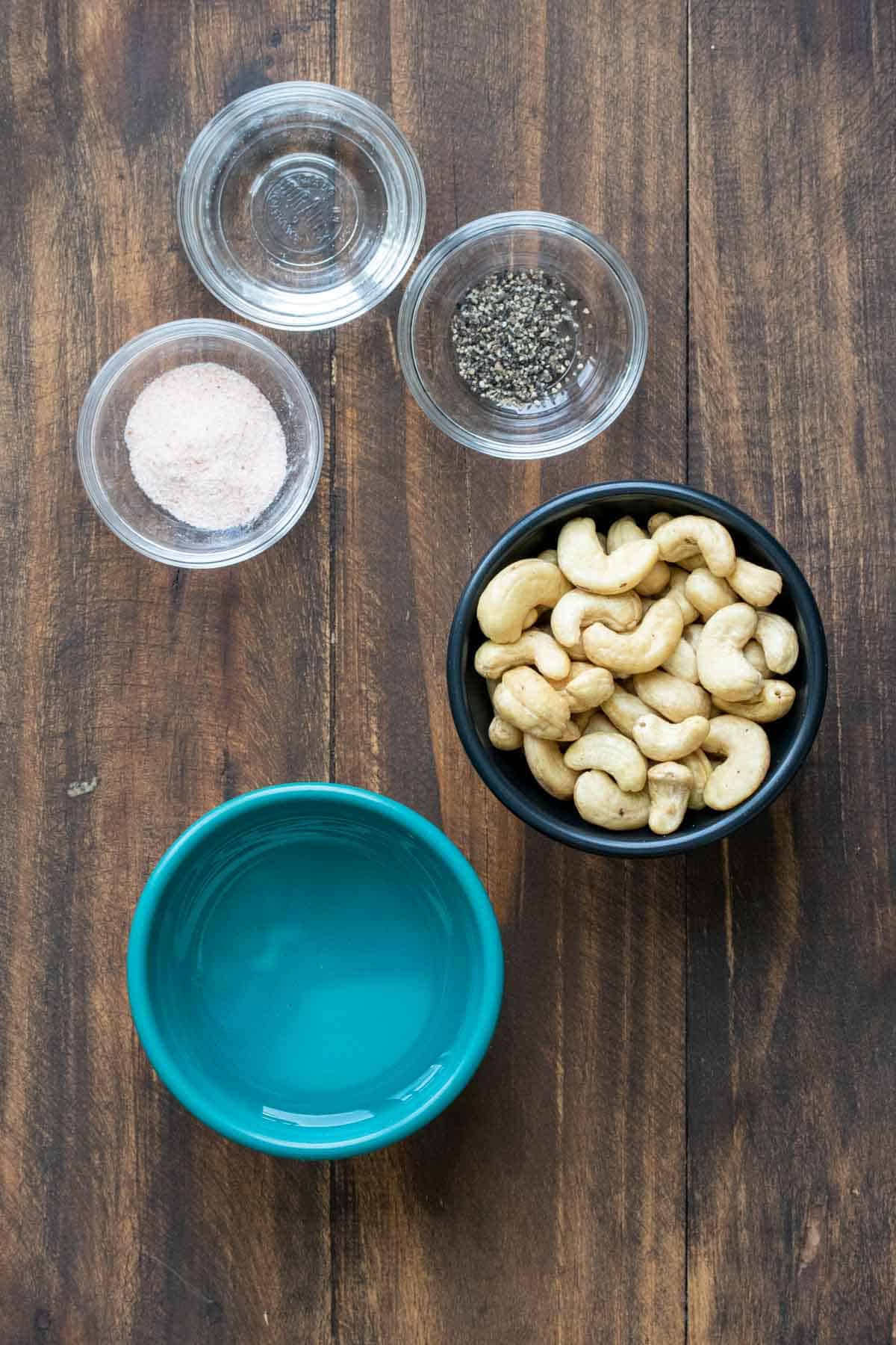 Bowls with cashews, water, salt, pepper and vinegar on a wooden surface