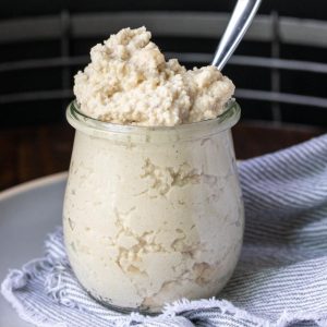 Glass jar filled with ricotta and a spoon in it.