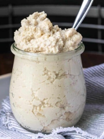 Glass jar filled with ricotta and a spoon in it.