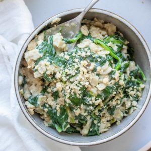 Grey bowl with spinach oatmeal and a metal spoon in it.