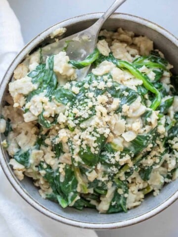 Grey bowl with spinach oatmeal and a metal spoon in it.