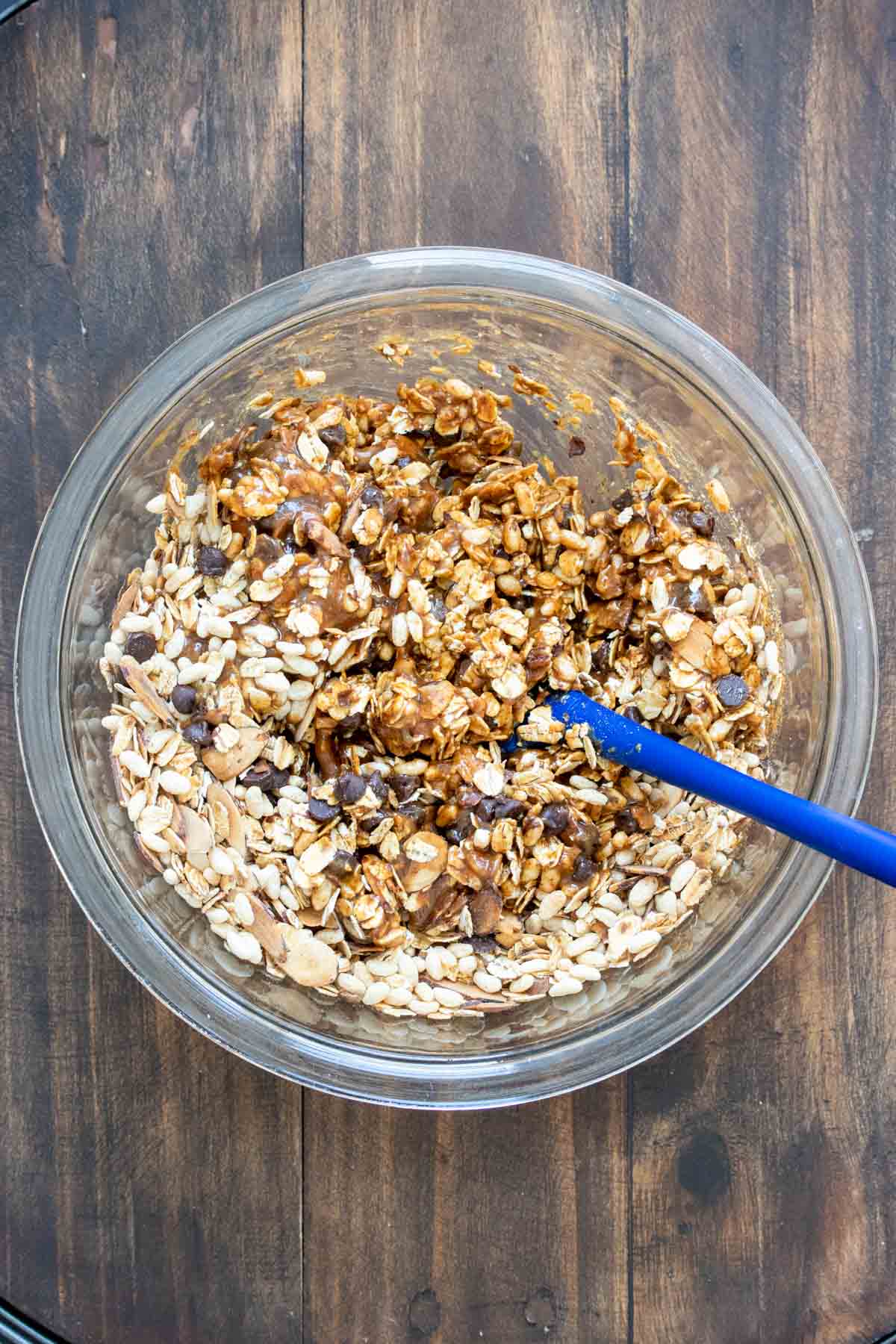 Spatula mixing oats and a brown sticky mixture in a bowl