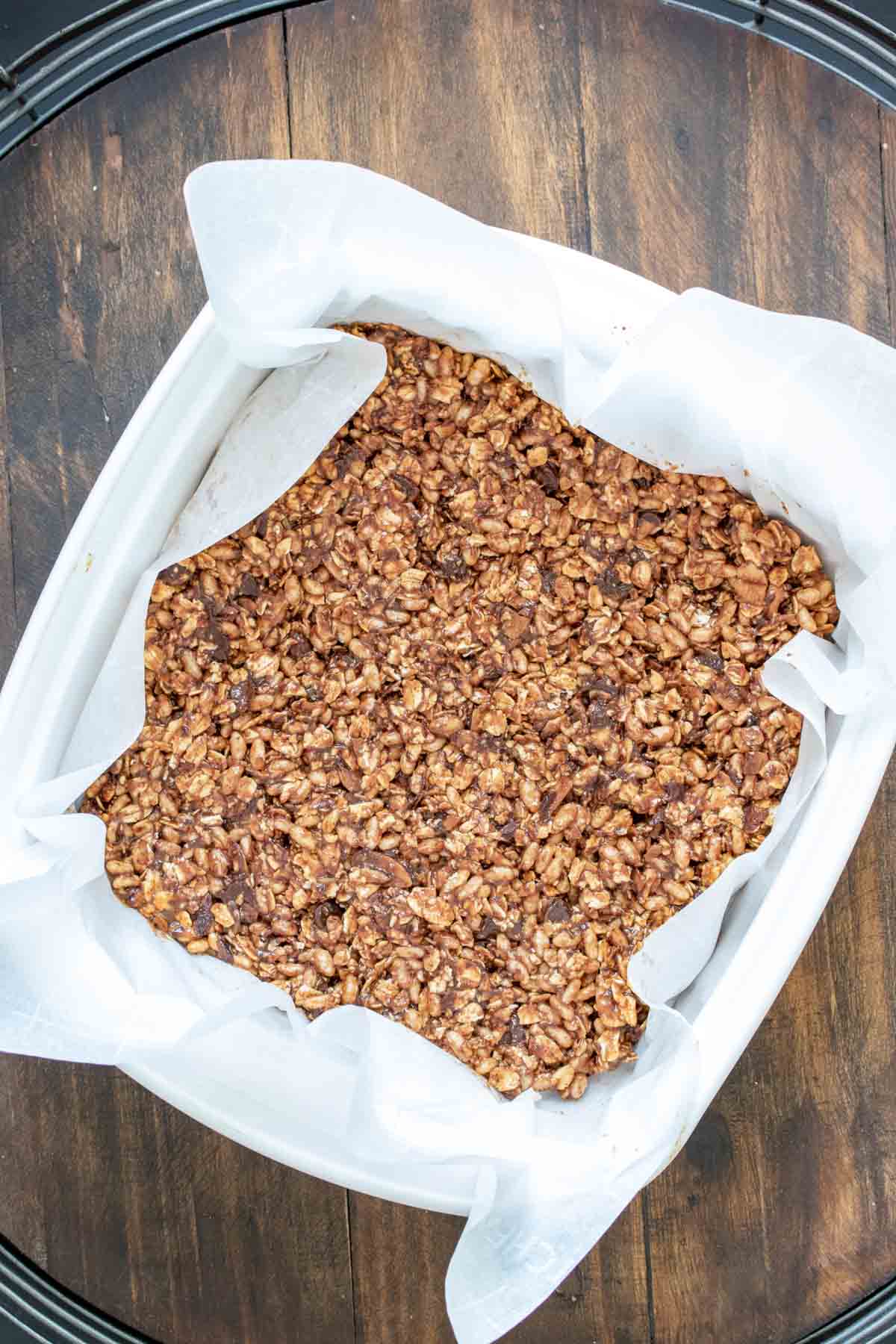 A granola bar mixture pressed into parchment paper in a glass pan