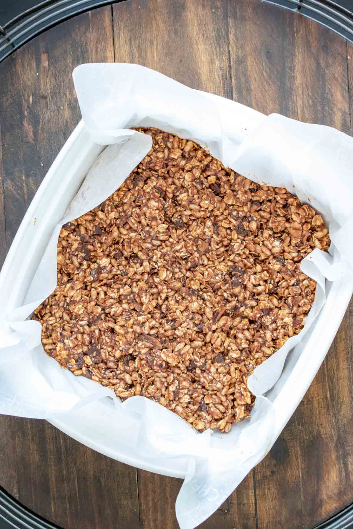 A granola bar mixture pressed into parchment paper in a glass pan