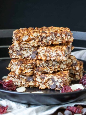 A stack of granola bars on a black plate with dried fruit and nuts
