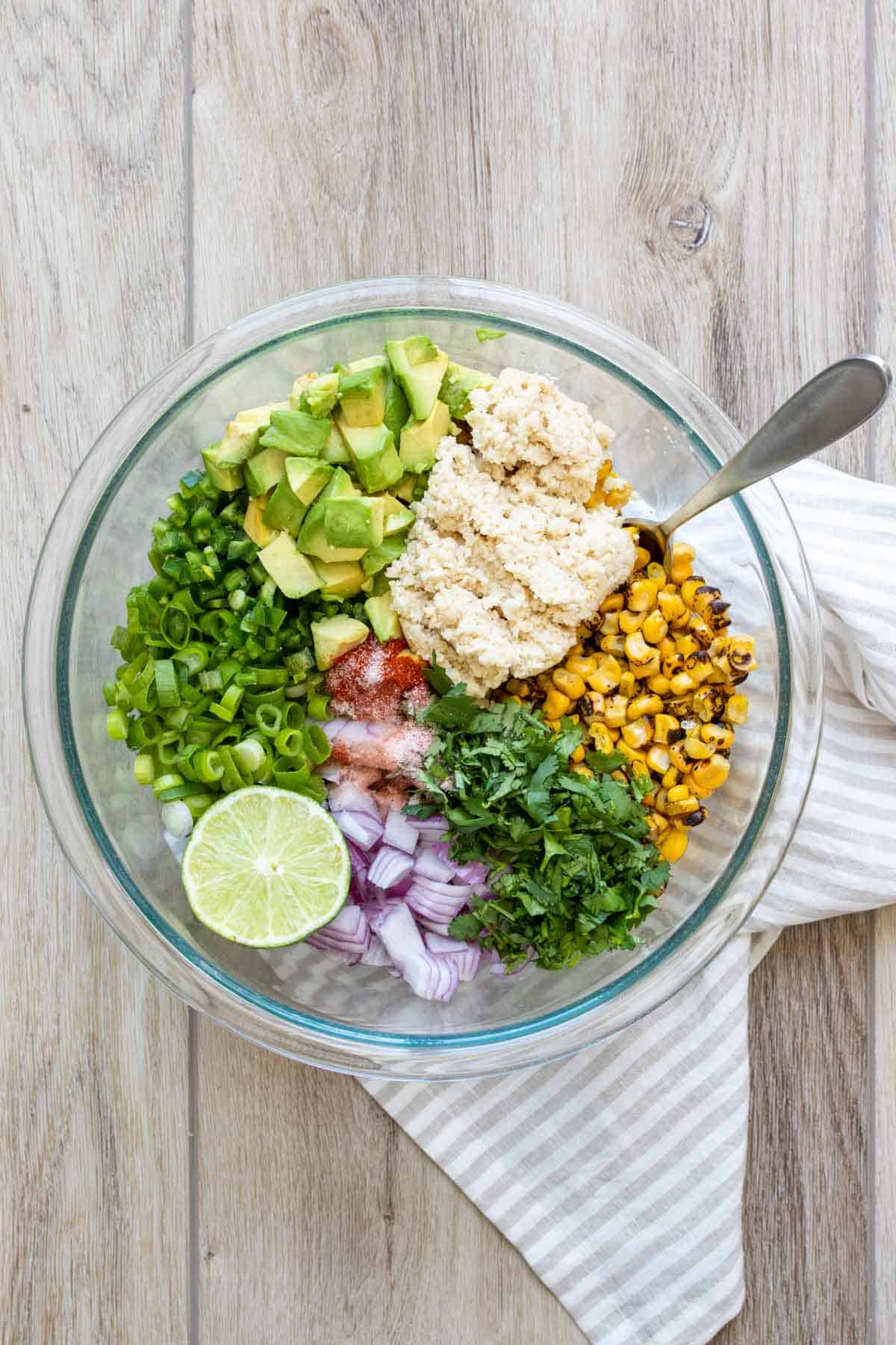 A glass bowl with ingredients to make a corn salad piled in.