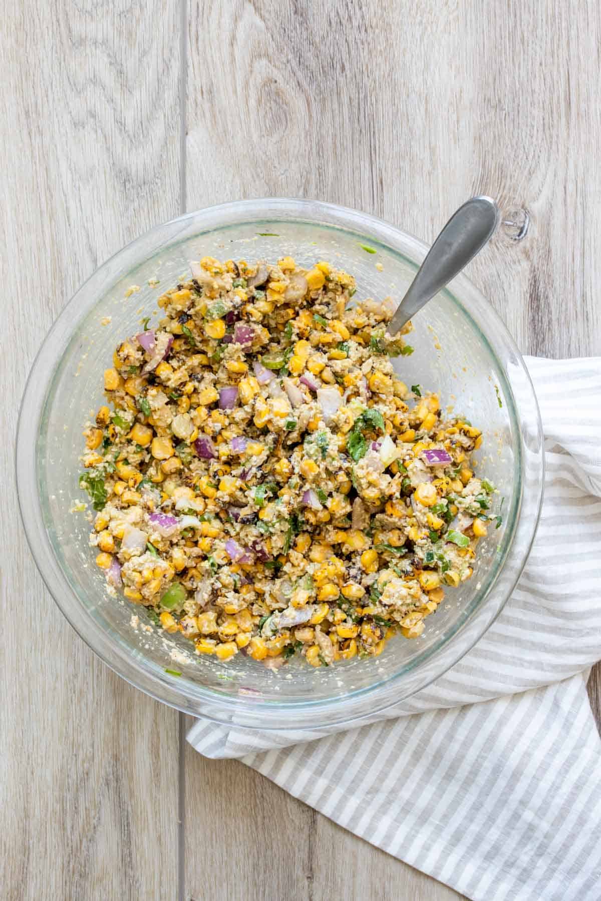 A glass bowl with mixed up corn salad inside.