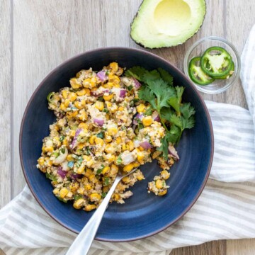 Corn salad with red onion and cilantro in a blue bowl next to avocado and jalapenos
