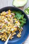 Dark blue bowl filled with corn salad and a sprig of cilantro