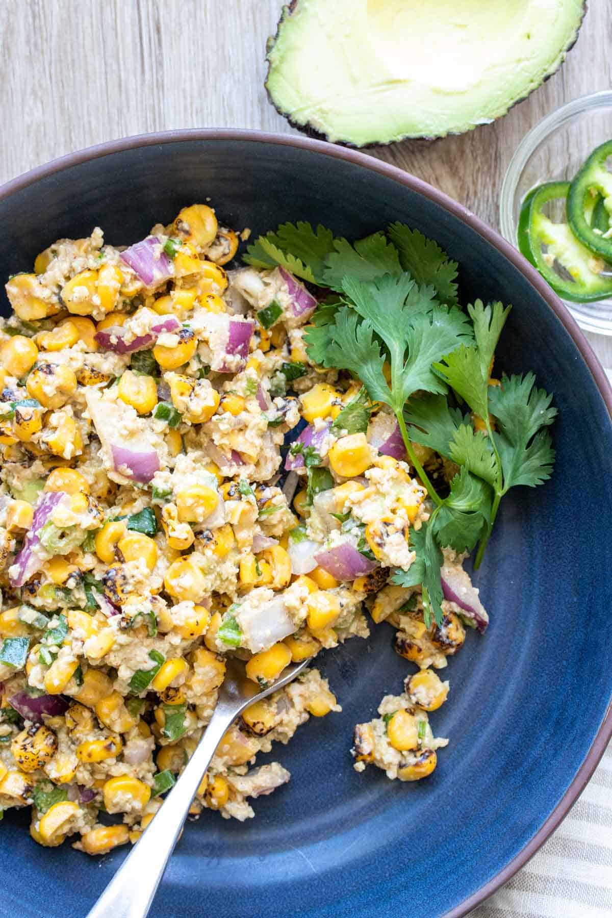 Dark blue bowl filled with corn salad and a sprig of cilantro.