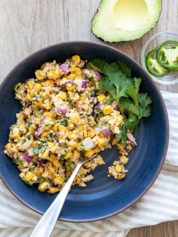 A blue bowl sitting on a striped towel with a corn salad in it and a spring of cilantro on the side.