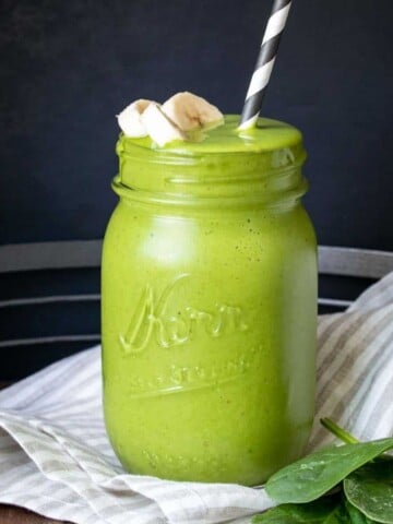 A green smoothie in a glass jar with banana slices on top and a straw