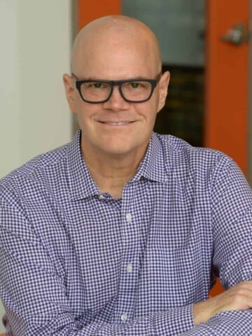 A bald man with glasses and a blue checkered button down shirt