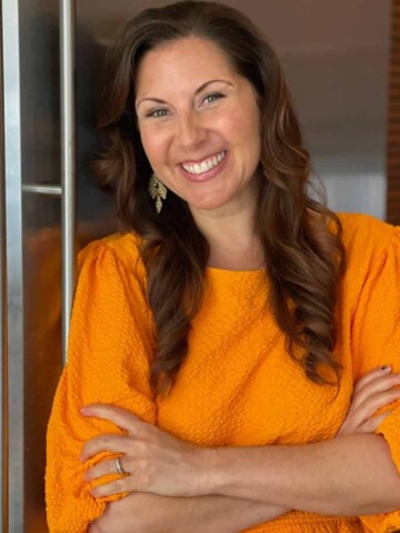 Woman in an orange dress crossing her arms and smiling at the camera