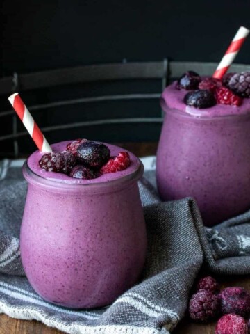 Two jars with purple smoothies and berries on top and red and white straws inside