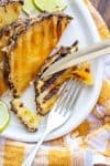 Fork and knife cutting a slice of grilled pineapple on a white plate