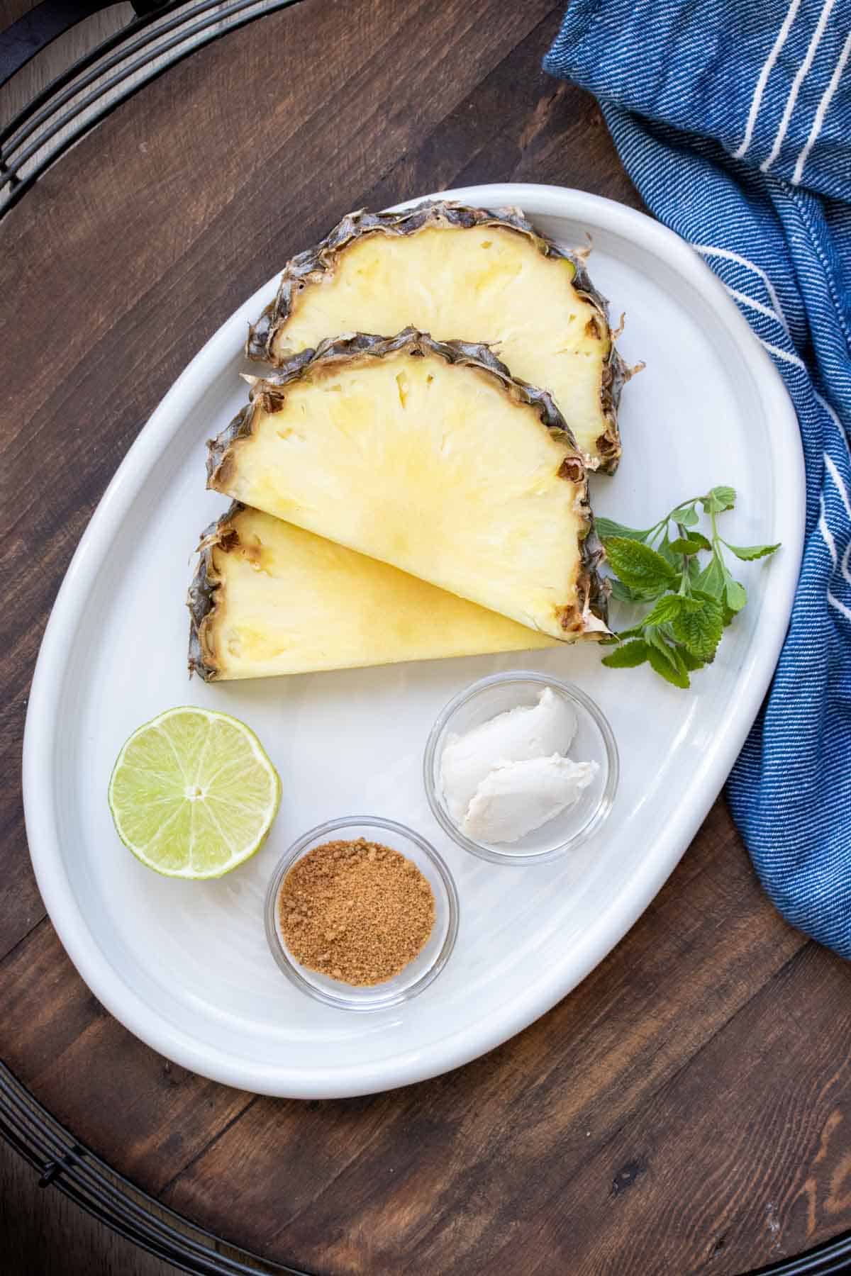 A white plate with slices of pineapple, lime, sugar, butter and mint.