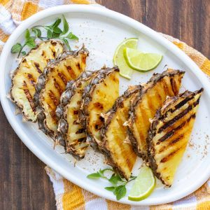 White platter filled with slices of grilled pineapple and garnished with lime and mint.