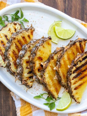 White platter filled with slices of grilled pineapple and garnished with lime and mint.