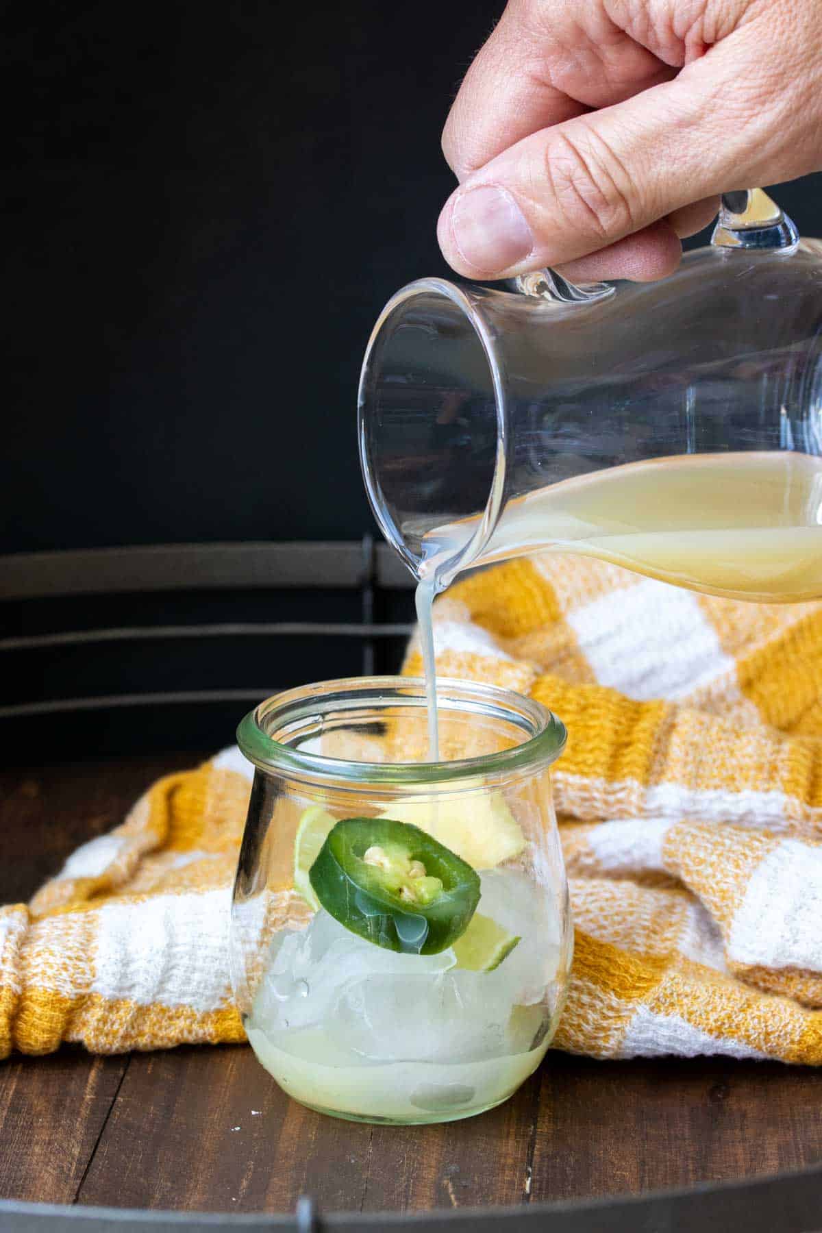 Hand pouring pineapple juice into a glass jar with a jalapeño in it