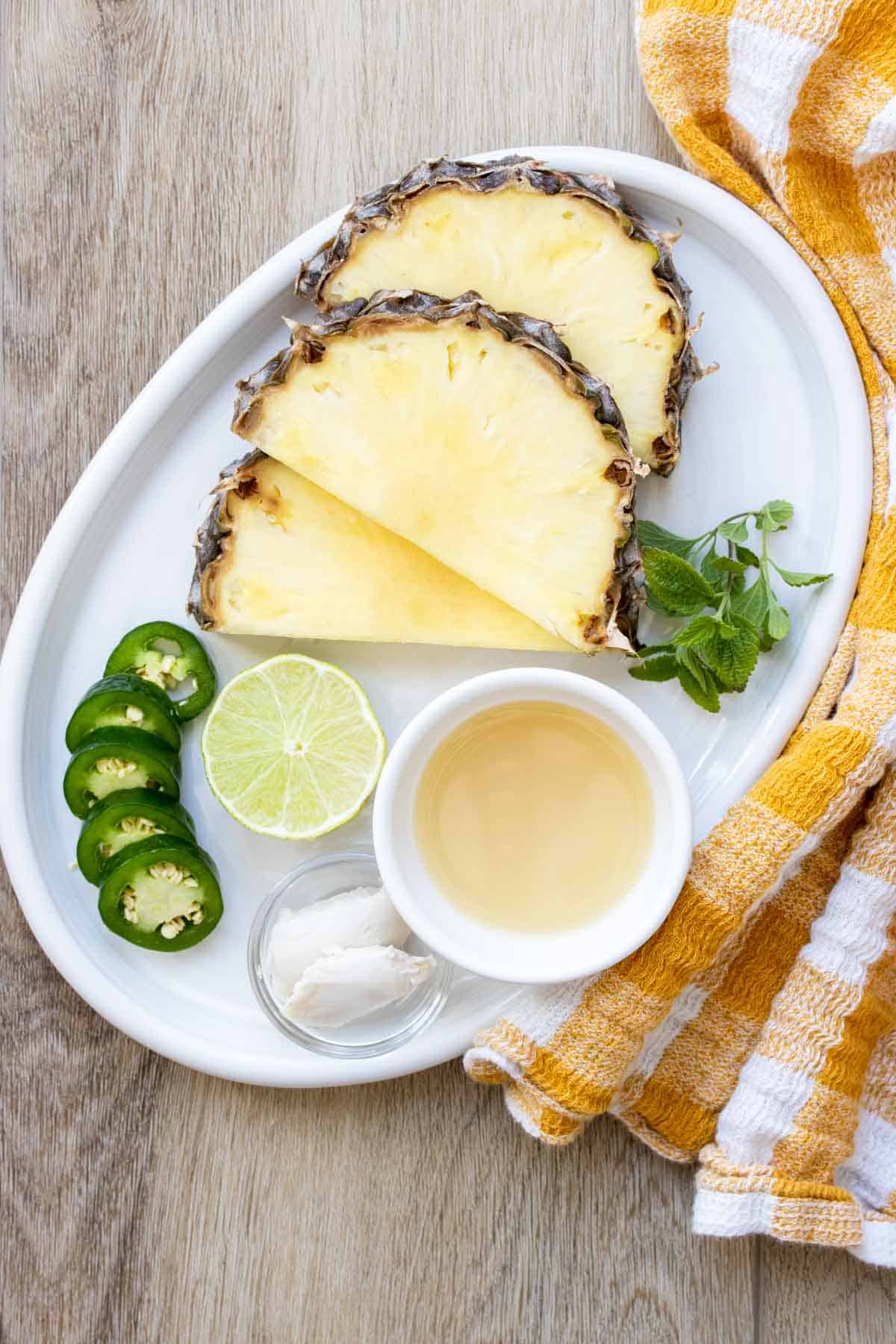 White platter with slices of pineapple and jalapenos, lime and juice