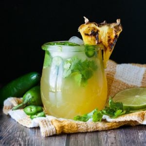 Glass jar with a pineapple on it's rim and a yellow cocktail inside