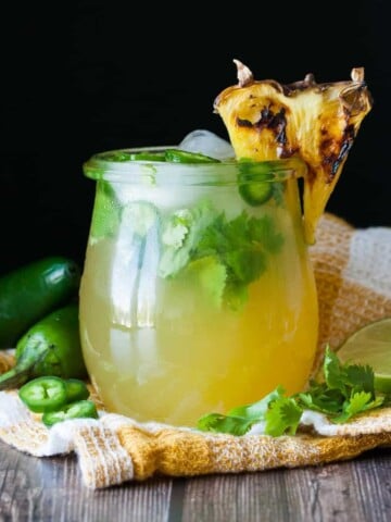 Glass jar with a pineapple on it's rim and a yellow cocktail inside