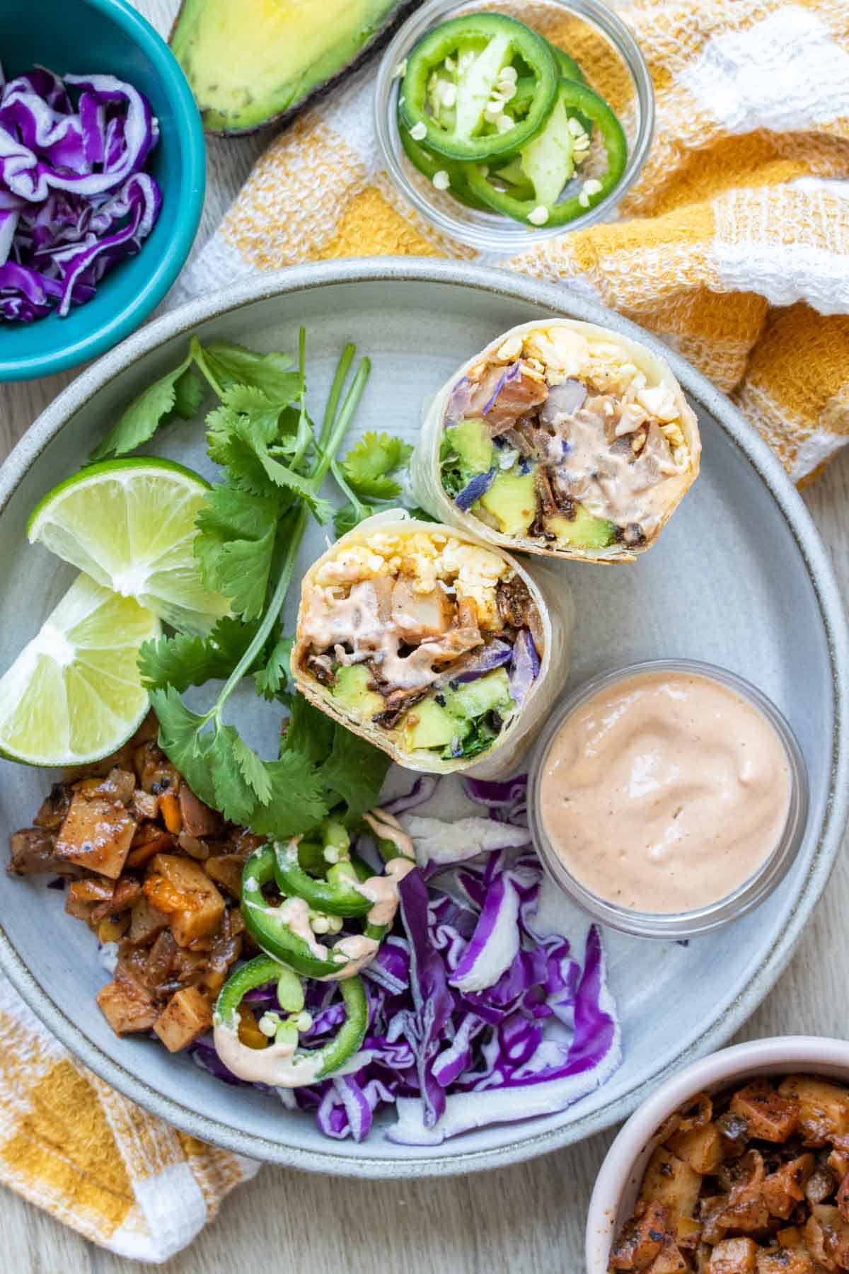 A breakfast burrito cut in half and sitting on a grey plate next to other ingredients