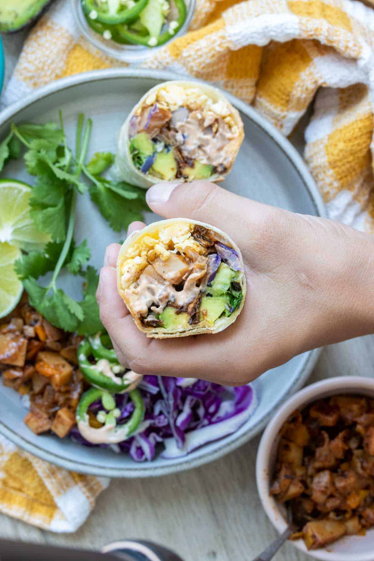 A hand holding a breakfast burrito cut side up over a grey plate.