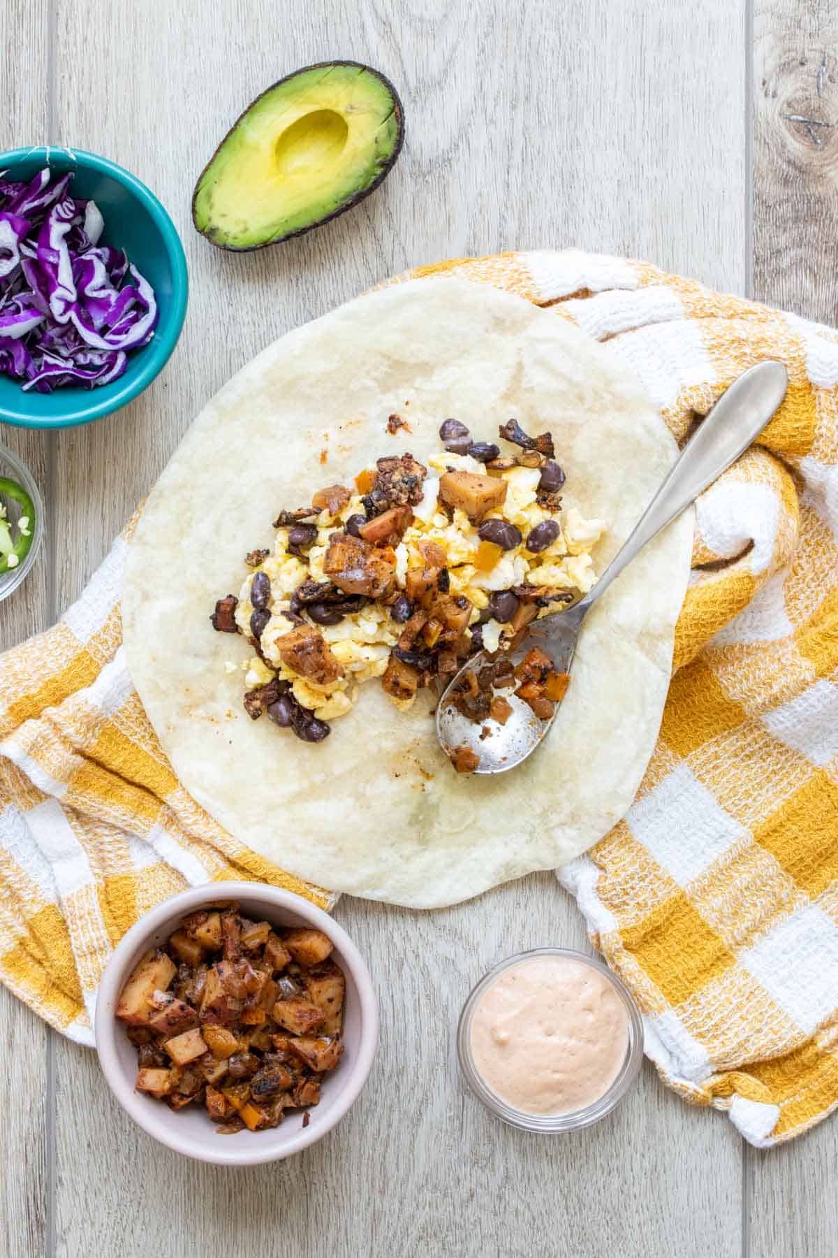 A tortilla with eggs and bacon being put on it.